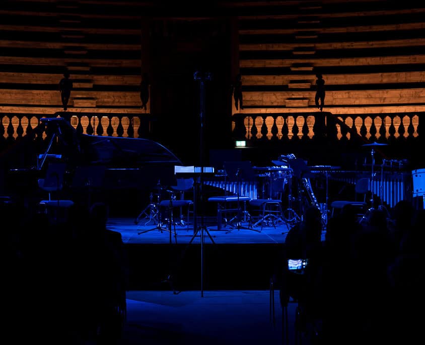 20260519 - 0002 Un palco con strumenti musicali in un ambiente teatrale con illuminazione blu scuro.
