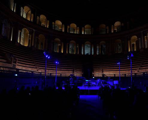 20260519 - 0003 Un palco vuoto in un teatro storico con luci blu e sedili in legno, pronto per un concerto musicale.