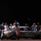Ragazzi e adulti in scena con un'auto d'epoca, scena di teatro musicale dal vivo.
