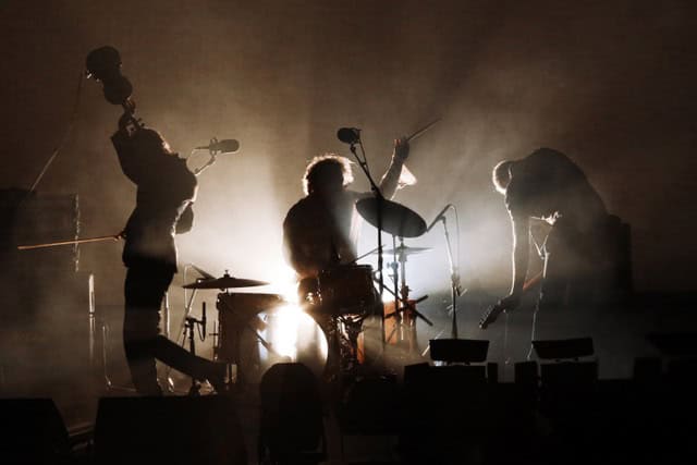 Dirty Three_SF 2016_credit Prudence Upton 059 Vita di scena di una band musicale dal vivo con luci soffuse e atmosfera intensa.