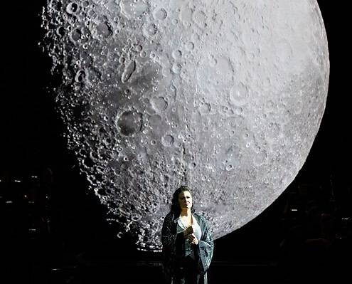 Luna gigante e donna sul palco Donna sul palco con luna gigante sullo sfondo, scena di musica e spettacolo.