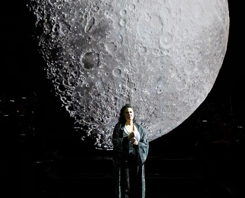 Luna gigante e donna sul palco Donna sul palco con luna gigante sullo sfondo, scena di musica e spettacolo.