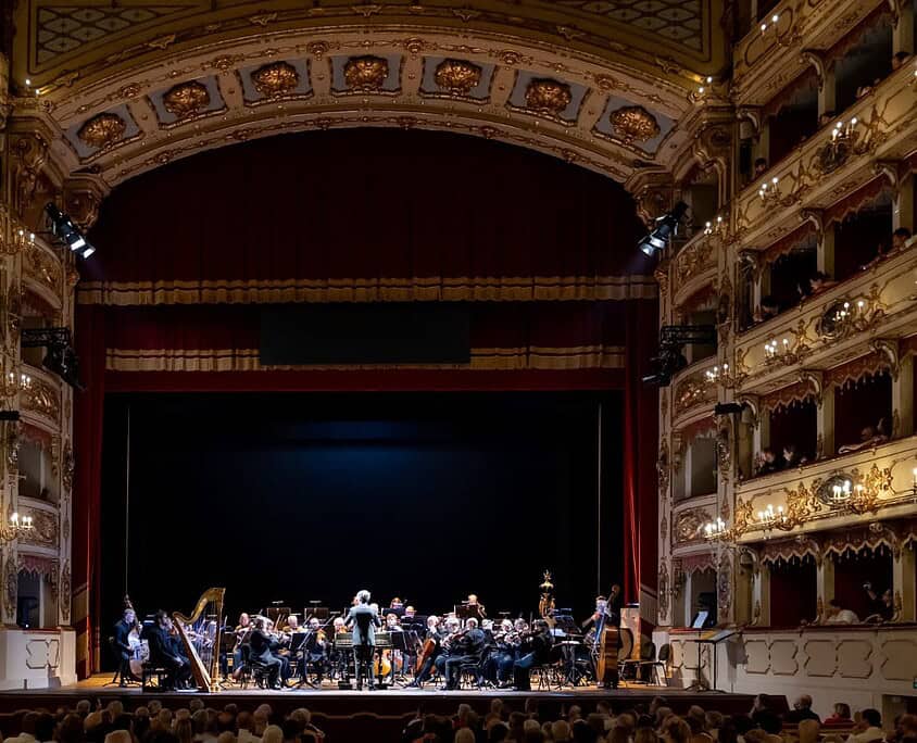 Orchestra sinfonica sul palco del Teatro Le Salon Musical, pronto per un concerto dal vivo.
